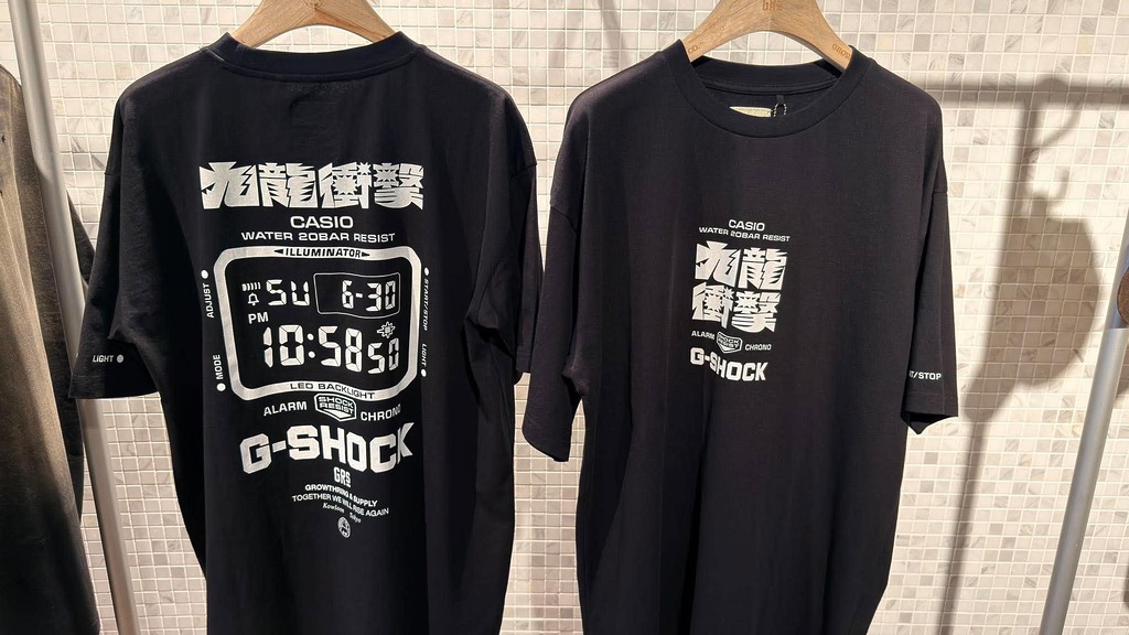 是次聯乘推出的黑色聯乘 T-Shirt ，正面印有簡約聯乘標誌，背面則大膽融入巨型電子錶面圖案及美山有操刀的「九龍衝擊」字樣，前後呼應手錶主題。